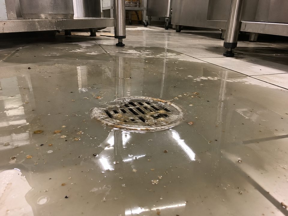 Sumidero de suelo atascado con agua estancada en una cocina comercial